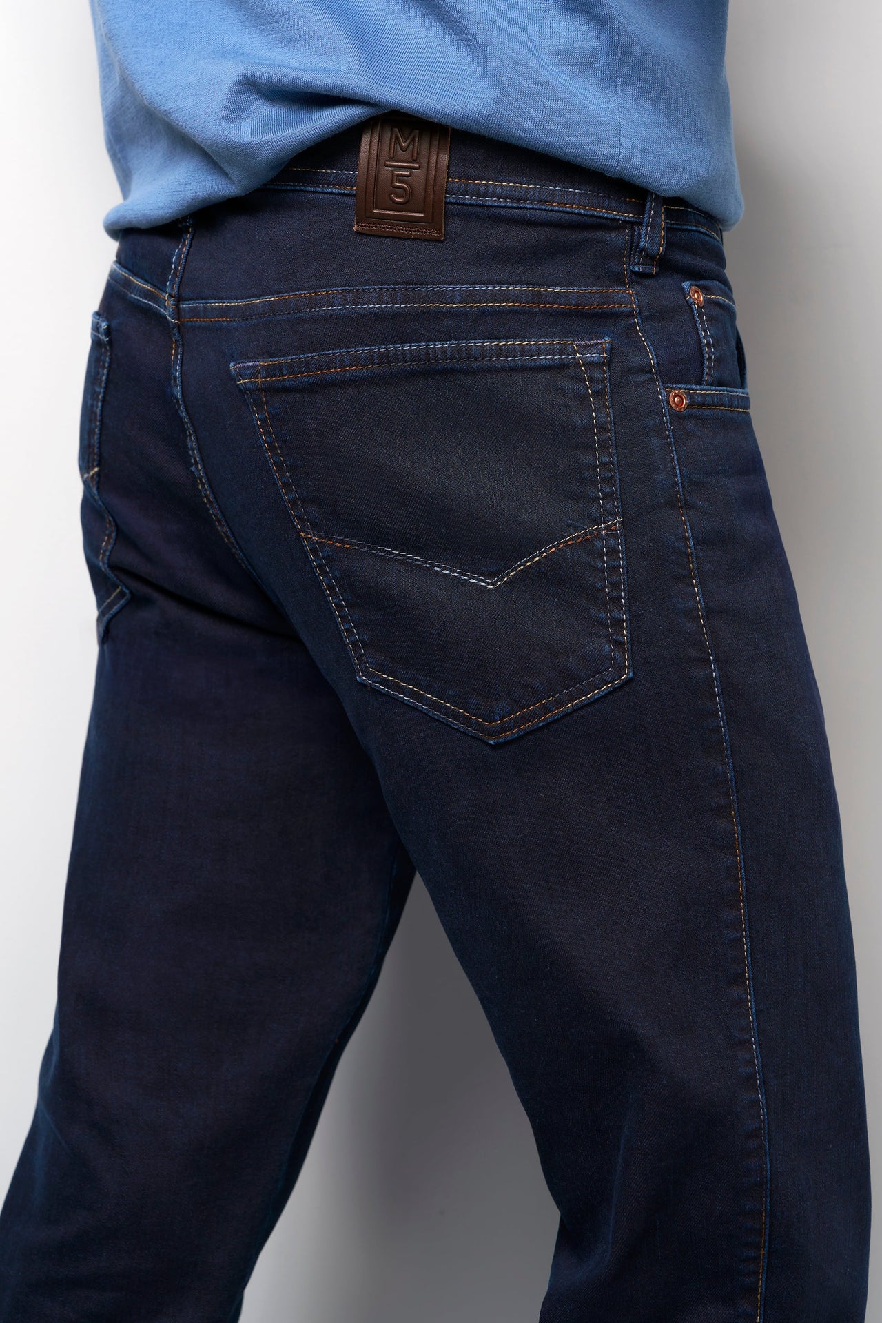 Dark blue jeans worn by a person on a plain background