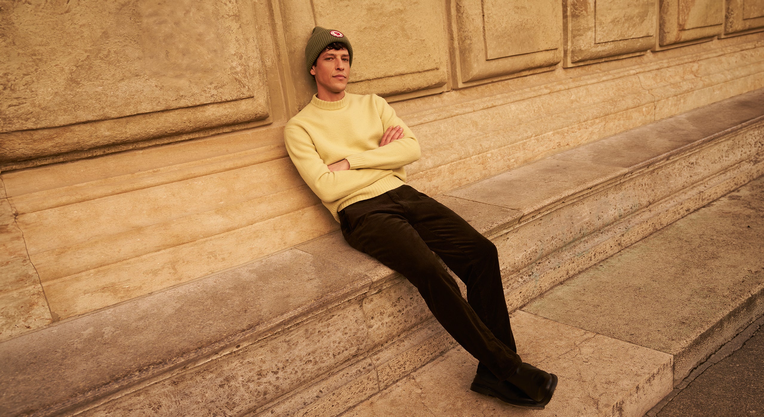 Person wearing a yellow sweater and green beanie sitting on stone steps.